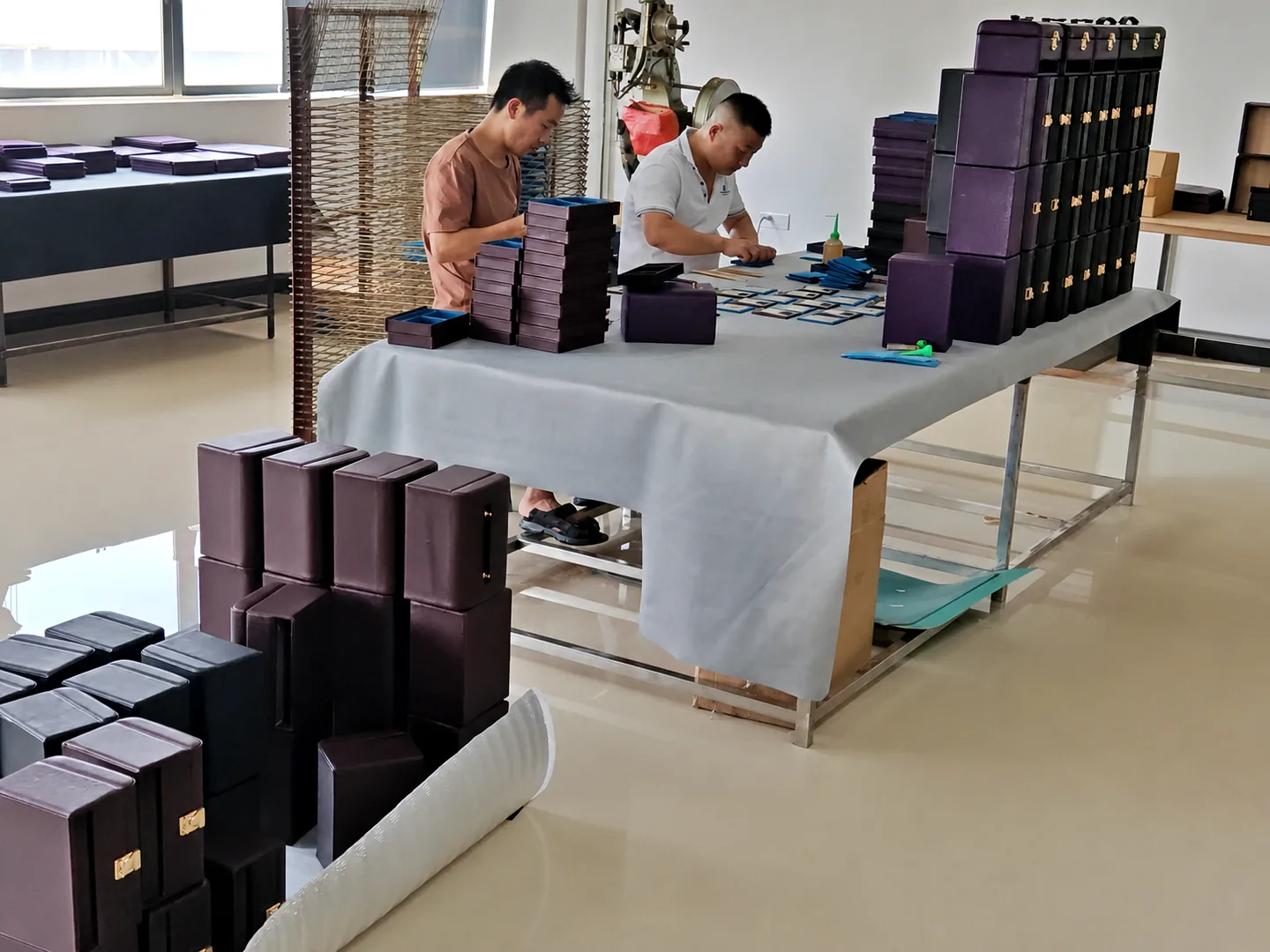 Two workers hand-assembling wrapped rigid boxes at a workbench