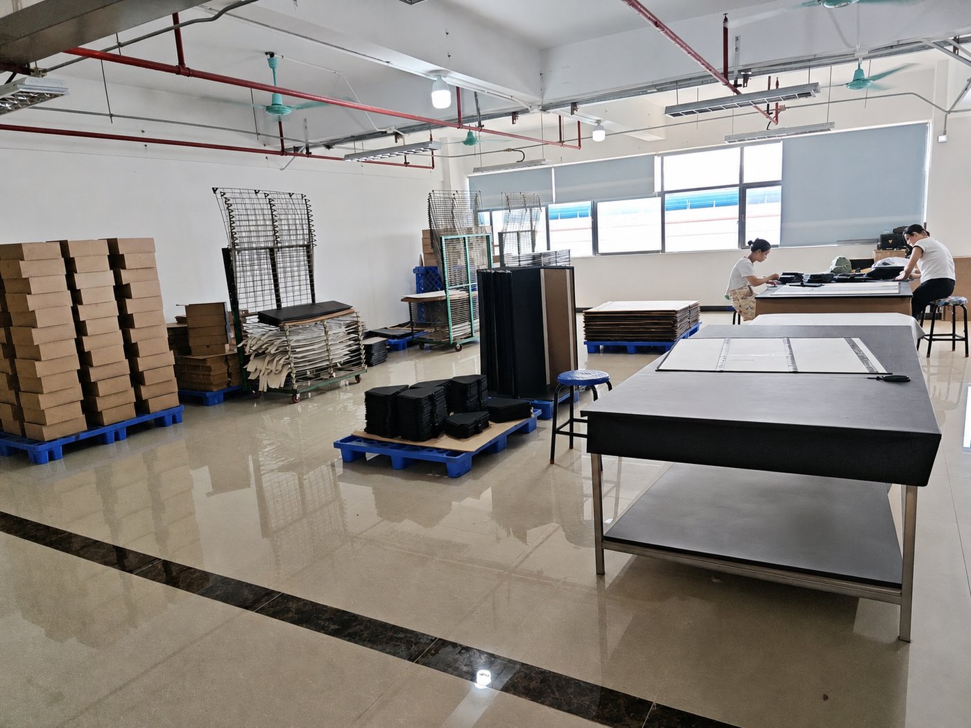 Materials and assembly area at DINLEEY with cut panels, pallets and workers preparing soft-goods components.