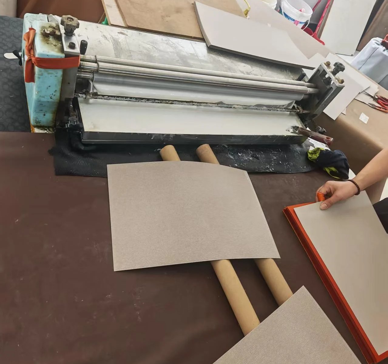 Glue roller machine with grey board panels and a wrapped board edge on the work table.