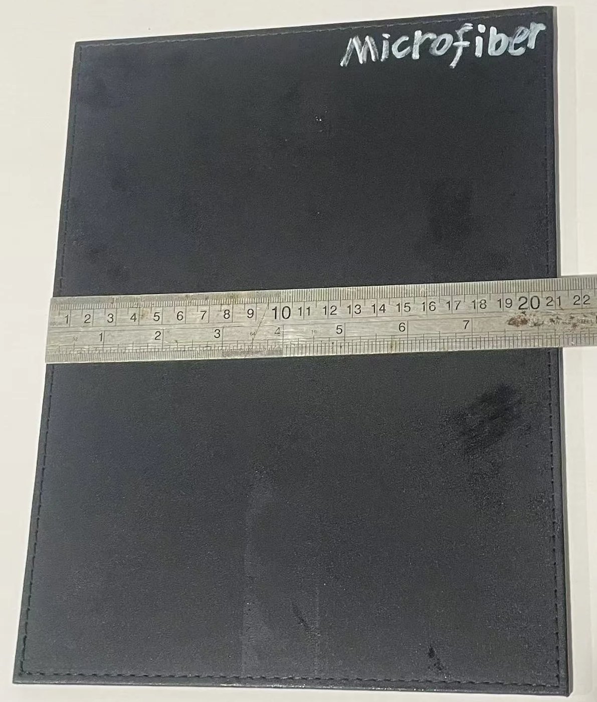 Stitched black microfiber material panel measured with a steel ruler during material matching.