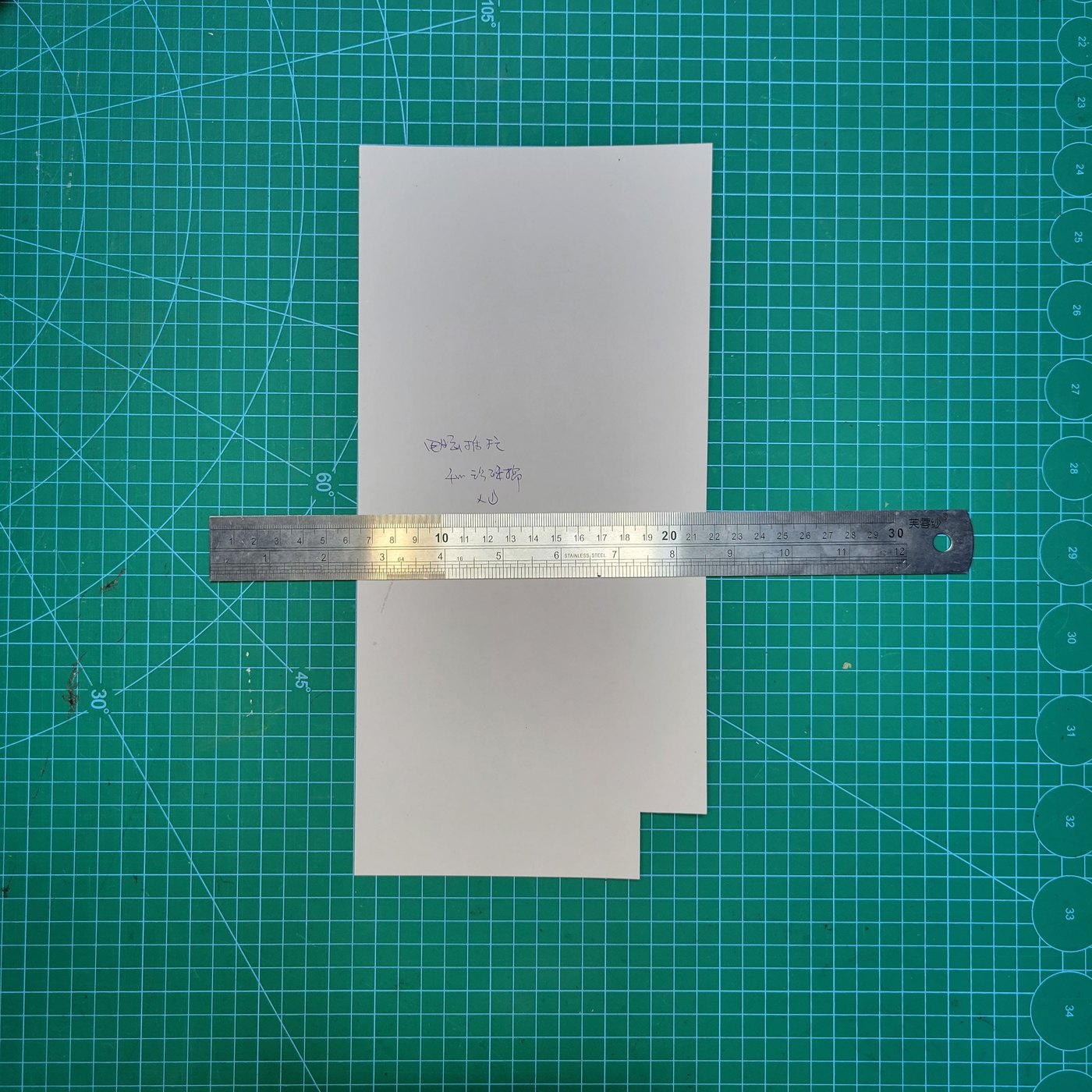 Paper pattern panel measured with a steel ruler on a green gridded cutting board during pattern making at DINLEEY.