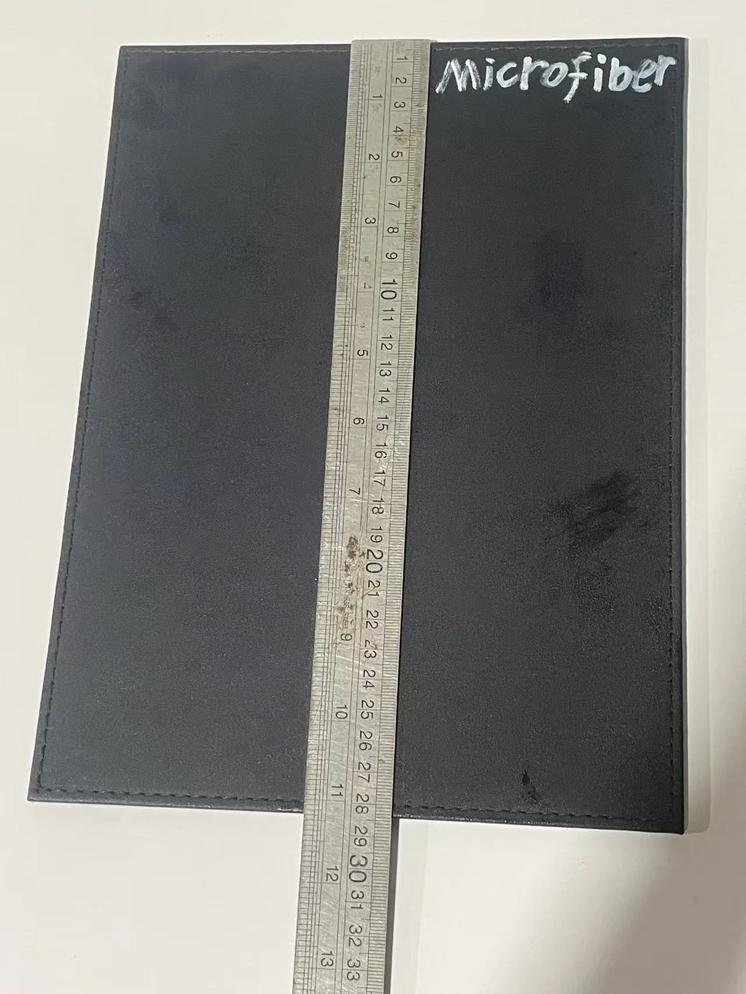 Black synthetic leather sample sheet with a steel ruler laid across it for measuring.