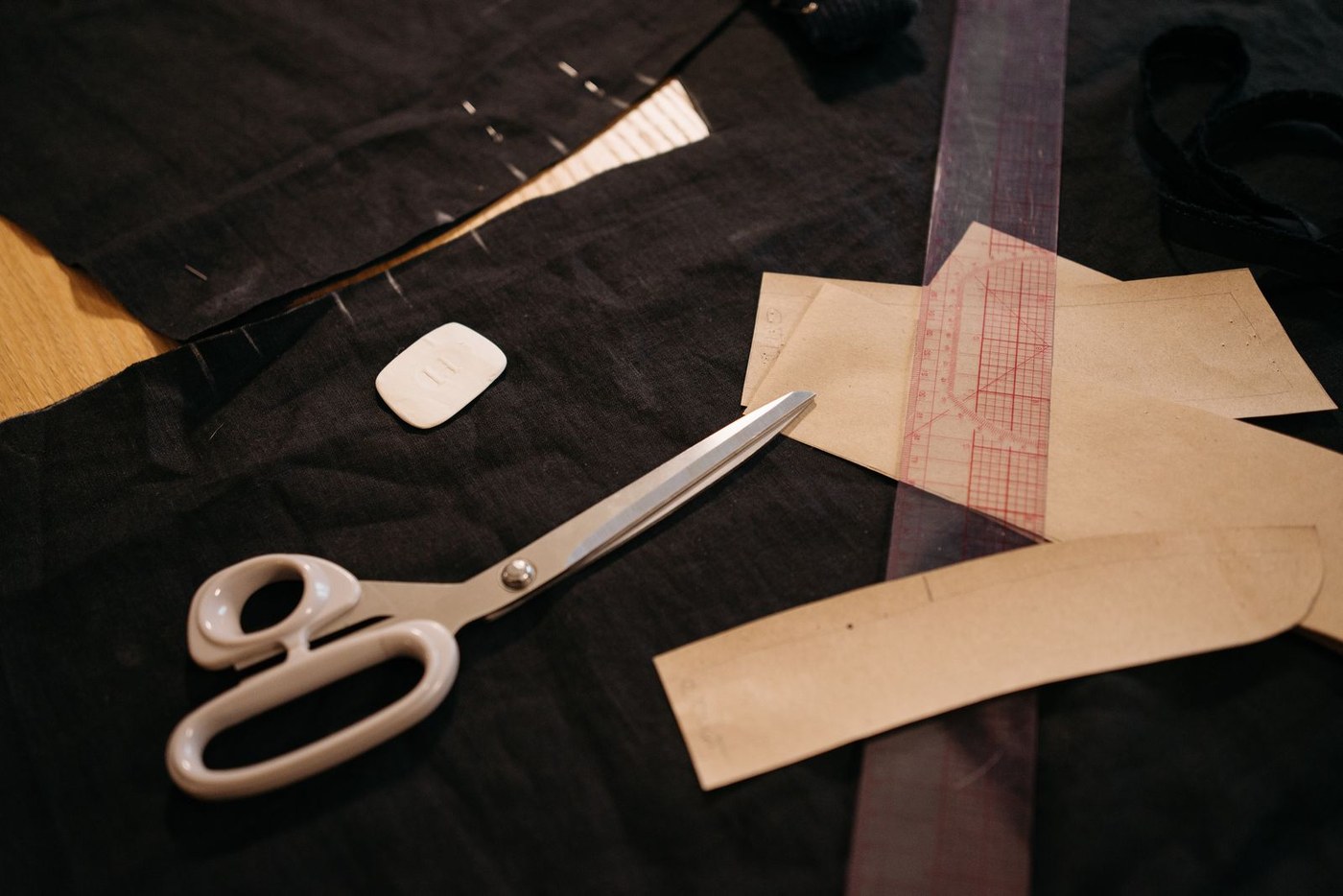 Scissors, chalk and paper pattern pieces on black fabric on a workbench.