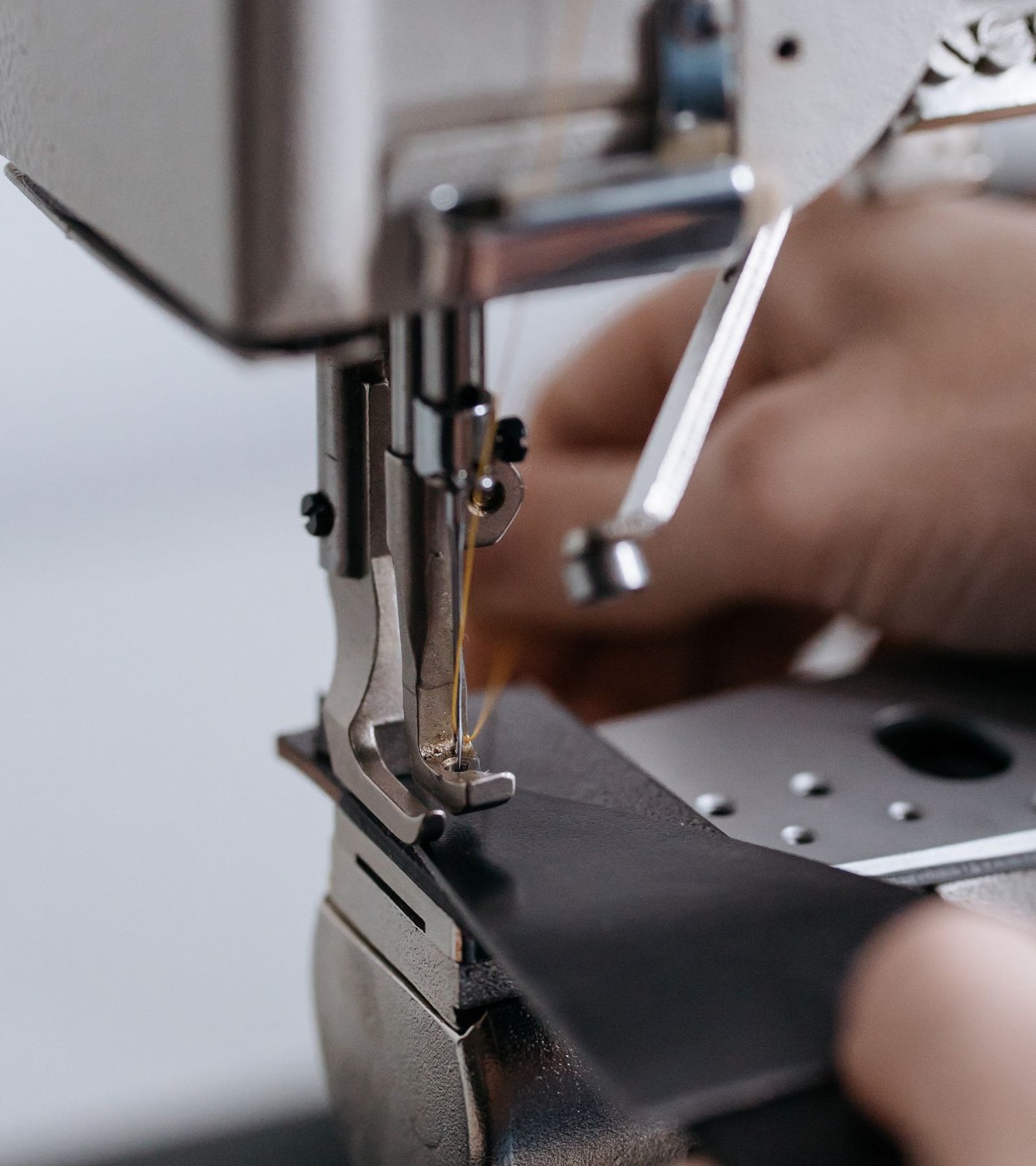 Hands guiding black material under the foot of an industrial sewing machine.