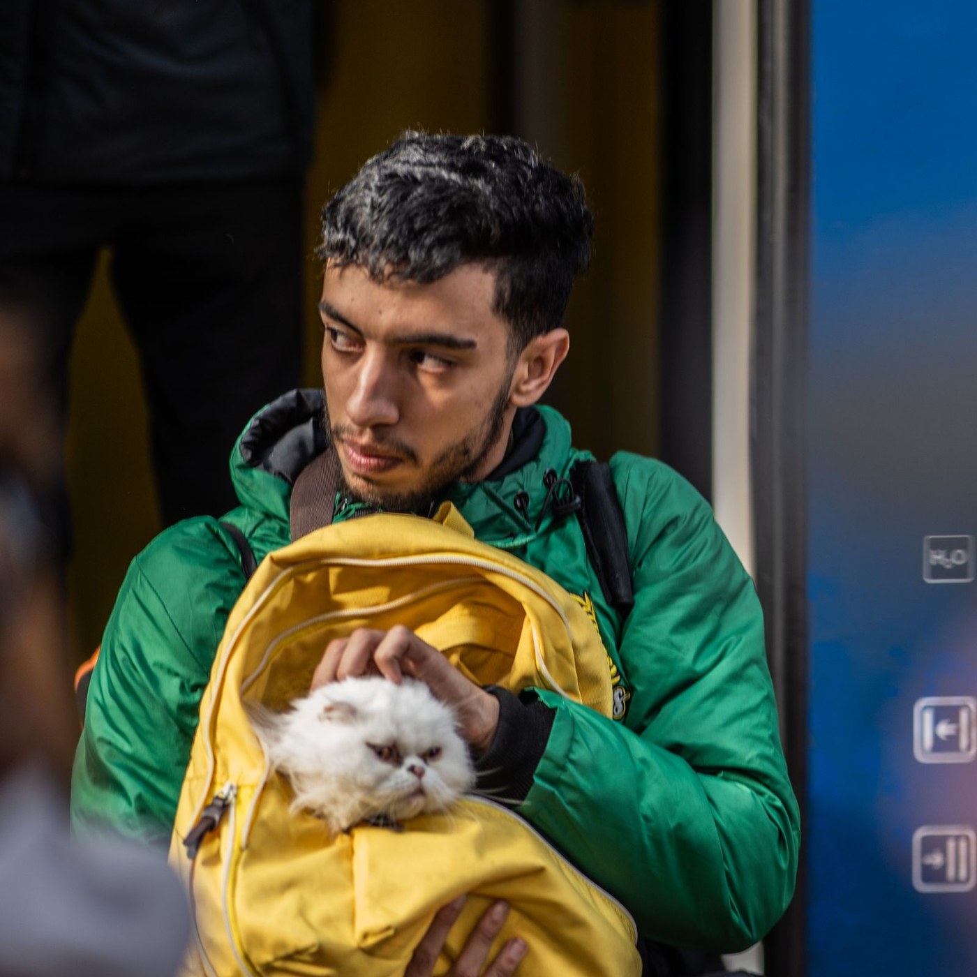 Man on a train holding a white cat in a yellow soft carrier bag.