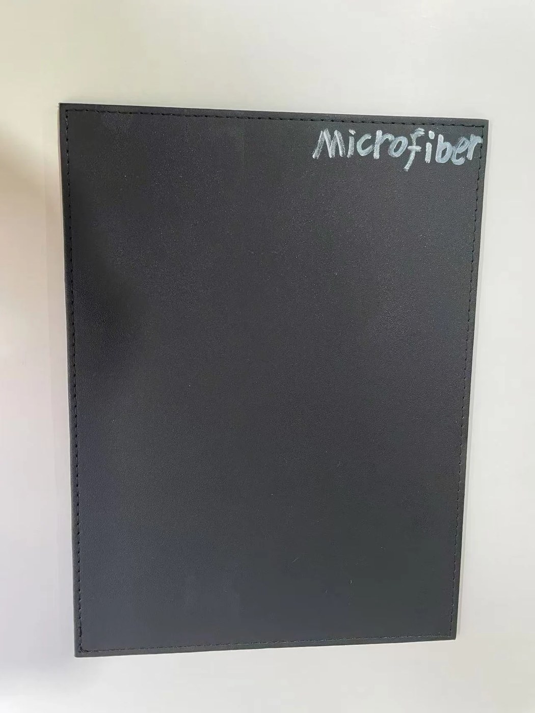흰 테이블 위 Microfiber라고 적힌 검은색 마이크로파이버 합성피혁 샘플 시트.
