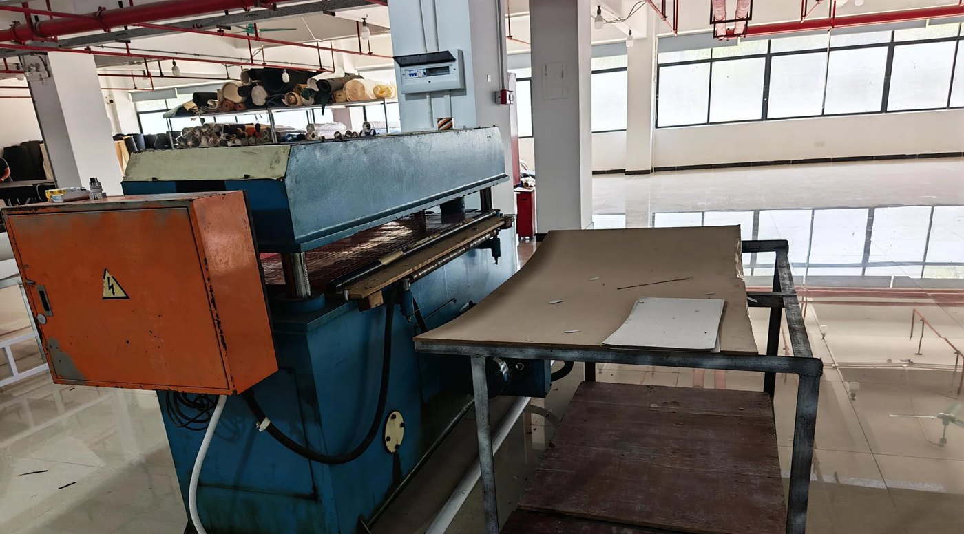Hydraulische Stanzpresse auf der Produktionslinie von DINLEEY, daneben eine zugeschnittene Platte auf dem Ablagetisch.