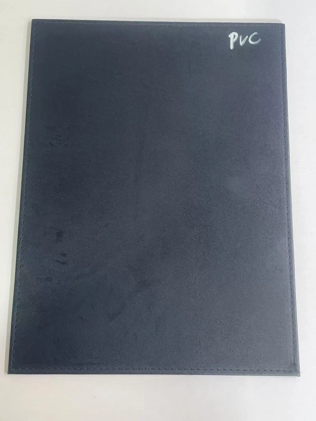 Schwarzer PVC-beschichteter Musterbogen mit der Aufschrift PVC auf einem weißen Tisch.
